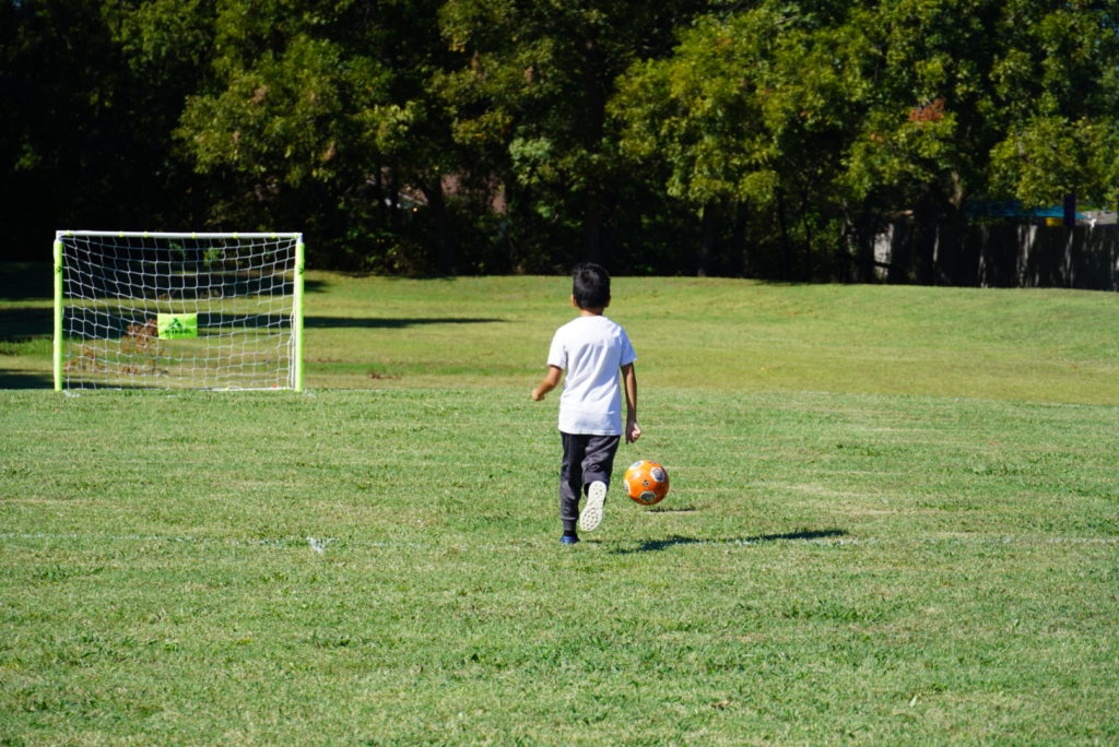 little boy kicking ball in field